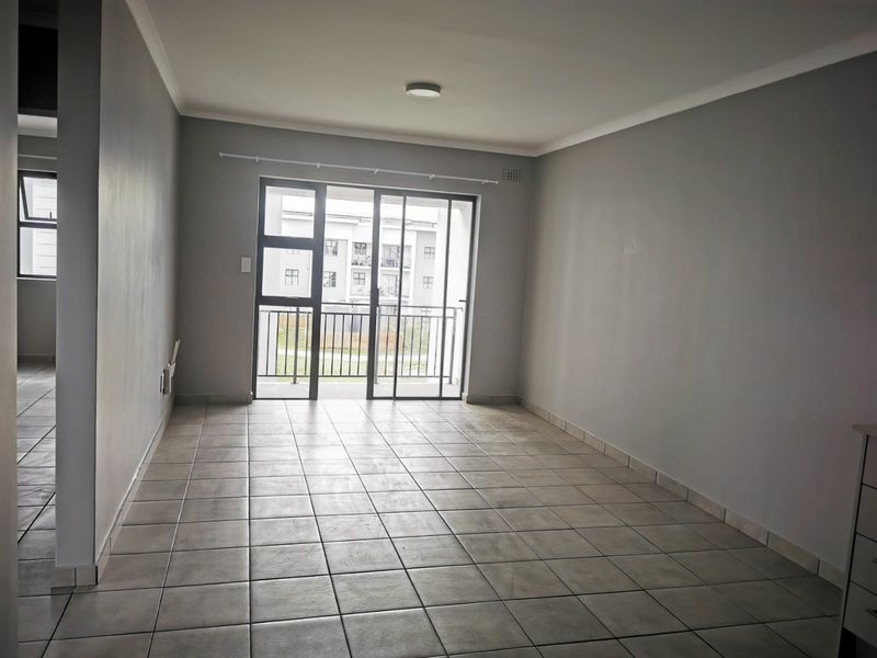 An empty, open-plan living area featuring neutral grey walls, tiled flooring, and a sliding glass door providing access to a balcony.