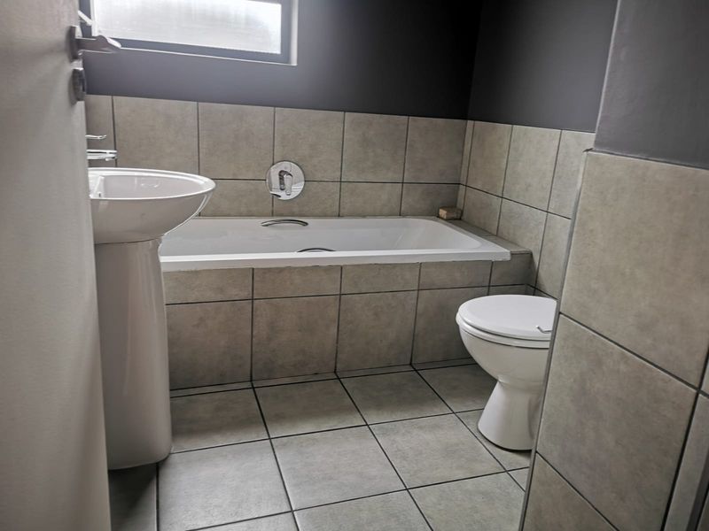 A functional bathroom featuring a pedestal basin, built-in bathtub, and toilet with neutral tiled finishes.