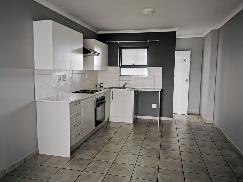 A clean, functional kitchen featuring white cabinetry, dark grey accent walls, tiled flooring, and built-in cooking appliances.