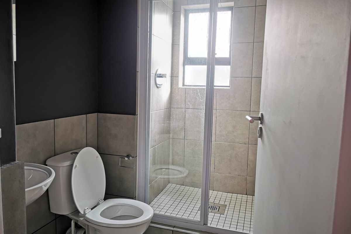 A functional bathroom featuring a shower enclosure, pedestal basin, and toilet with neutral wall and floor tiling.