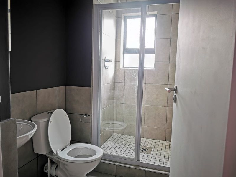 A functional bathroom featuring a shower enclosure, pedestal basin, and toilet with neutral wall and floor tiling.