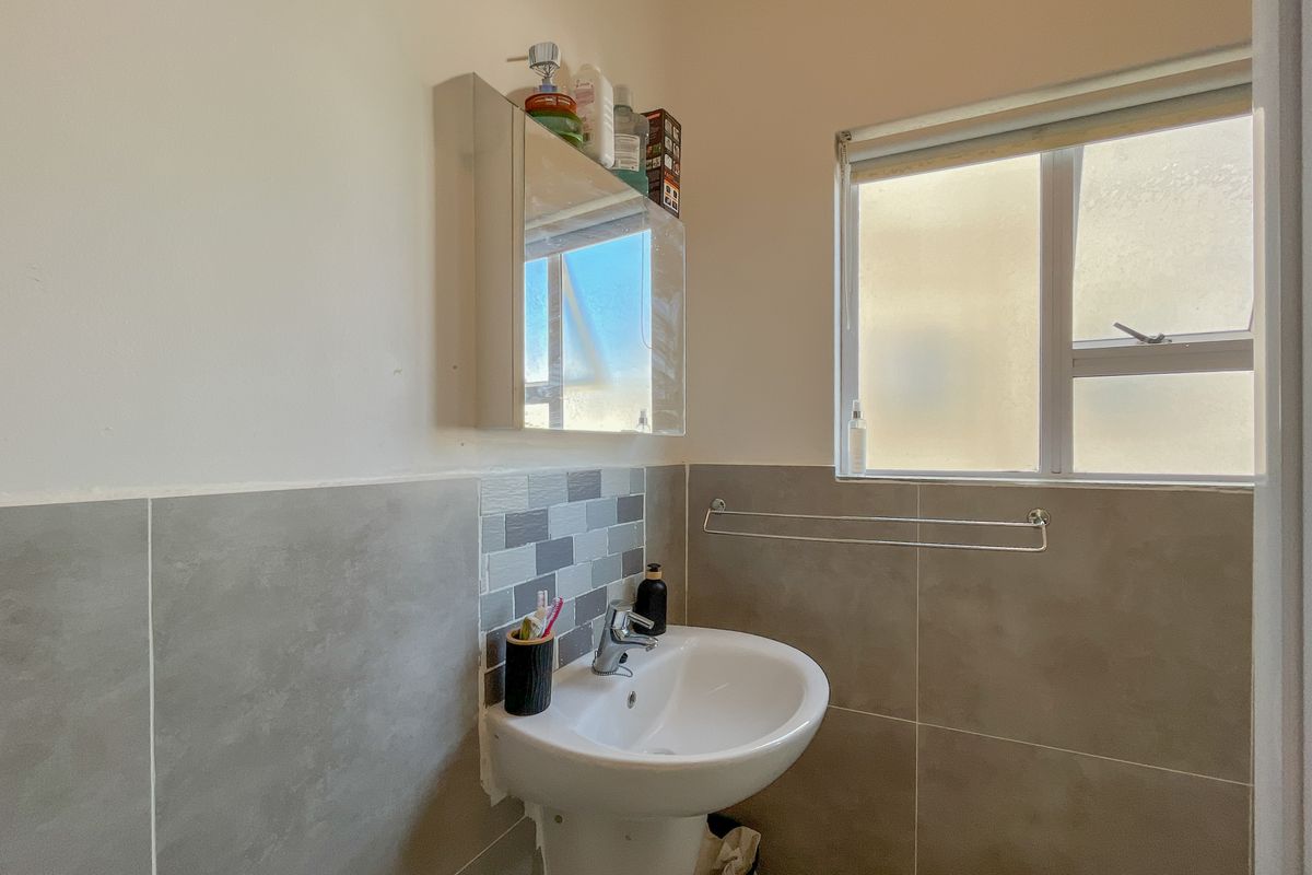 A functional bathroom featuring a pedestal basin with a mixer tap, tiled splashback, mirrored medicine cabinet, and a frosted glass window.