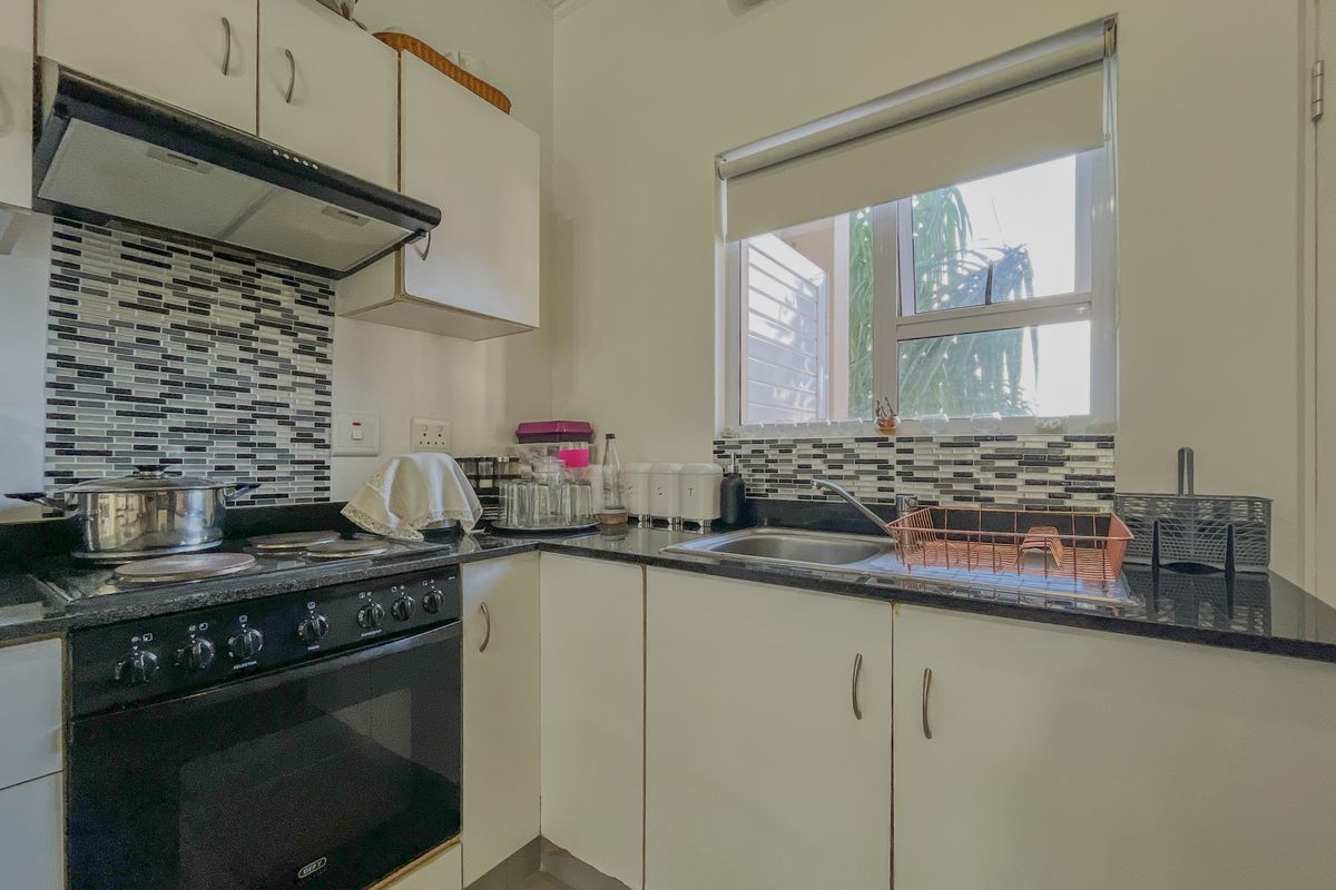 Compact kitchen featuring white cabinetry, granite countertops, mosaic tile backsplash, and integrated electric stove with extractor fan.