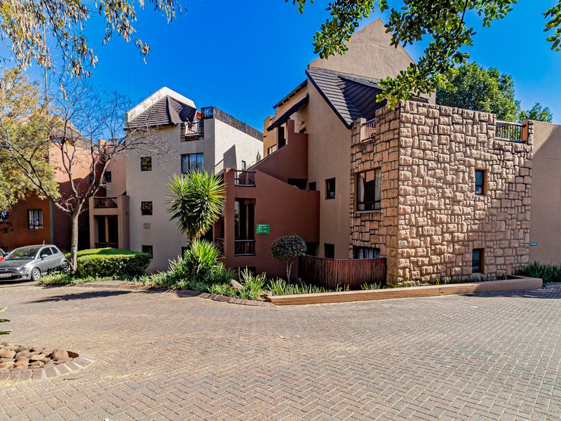 Exterior view of a multi-story apartment complex featuring stone cladding, paved driveway, and private balconies.
