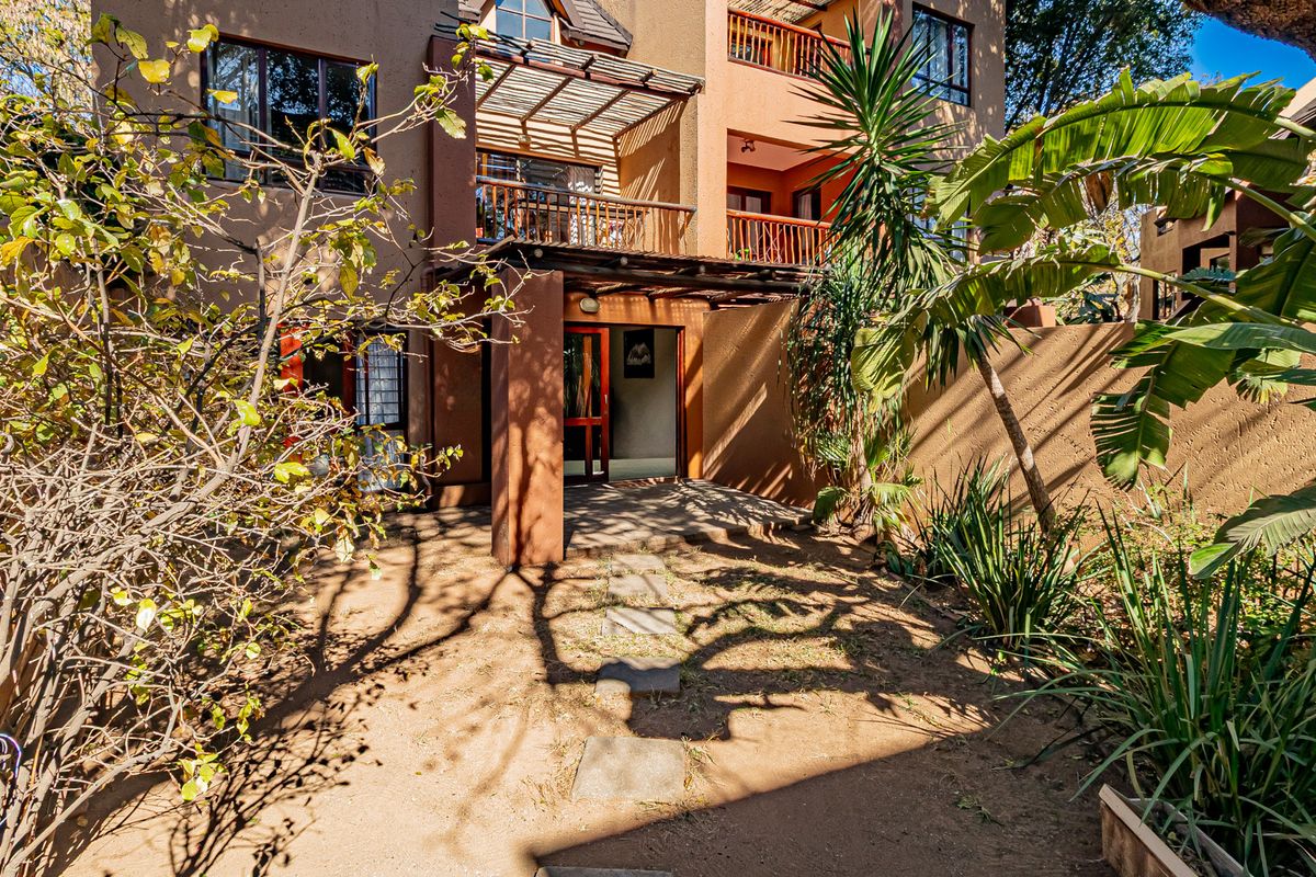 Rear view of the apartment featuring a covered patio, timber pergola, and a private garden area with a stone pathway.