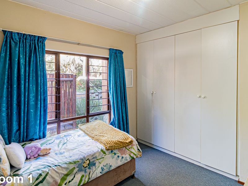 A bedroom featuring built-in cupboards, carpeted flooring, and a window fitted with security bars.