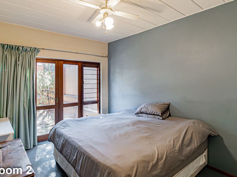 A bedroom featuring a ceiling fan, carpeted flooring, and a wooden framed glass door providing access to the exterior.