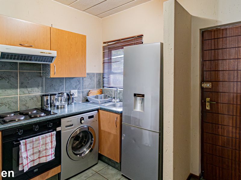 Compact kitchen featuring laminate cabinetry, built-in oven with hob, extractor fan, and integrated laundry plumbing, finished with tiled backsplash and flooring.