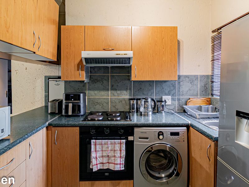 A compact kitchen featuring laminate cabinetry, built-in oven, electric hob, extractor fan, and integrated laundry facilities with a tiled backsplash.