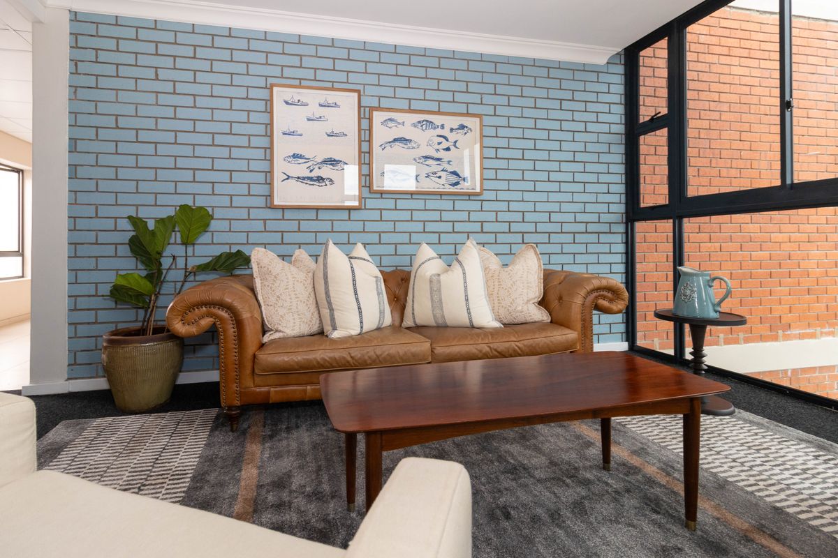 A well-lit living room featuring a distinctive blue painted brick feature wall and large black aluminium framed windows.