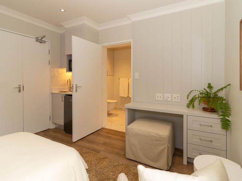 A well-appointed bedroom featuring a built-in desk, integrated kitchenette with sink, and direct access to an en-suite bathroom with modern finishes.