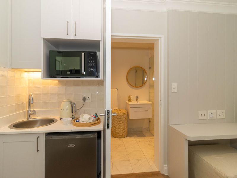 Compact kitchenette featuring white cabinetry, stone countertops, and integrated appliances, with an adjoining bathroom visible through the doorway.