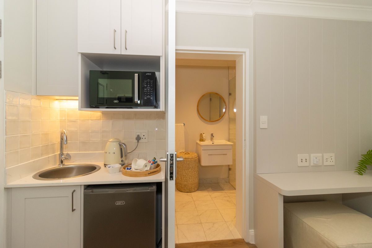 Compact kitchenette featuring white cabinetry, stone countertops, and integrated appliances, with an adjoining bathroom visible through the doorway.
