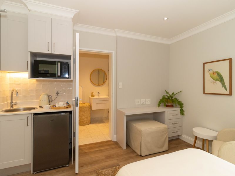 Compact open-plan studio featuring a kitchenette with built-in cabinetry and microwave, adjacent to a modern bathroom with a vanity and mirror.