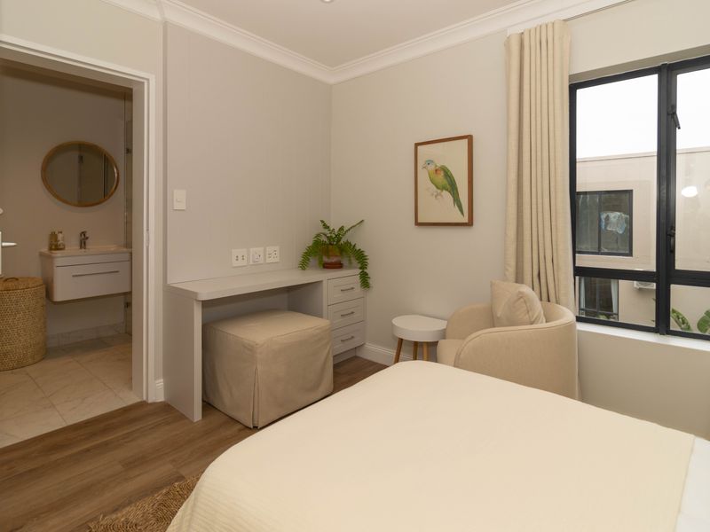 A well-maintained bedroom featuring laminate flooring, a built-in desk, and an adjoining en-suite bathroom with a modern wall-mounted vanity.