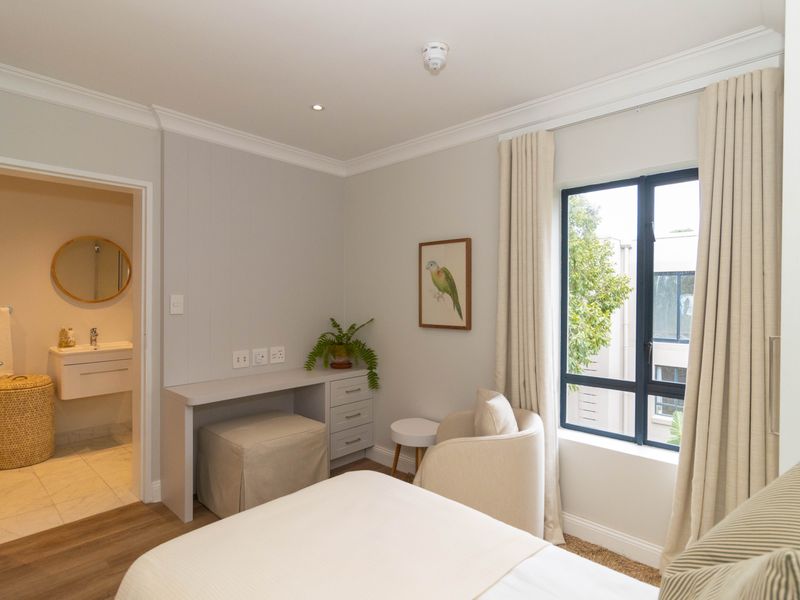 A well-maintained bedroom featuring a built-in desk, crown molding, and an en-suite bathroom with modern vanity and fixtures.