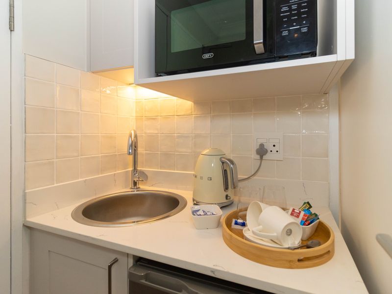 A compact, well-appointed scullery or kitchenette area featuring a stainless steel sink, stone countertop, tiled backsplash, and built-in microwave.