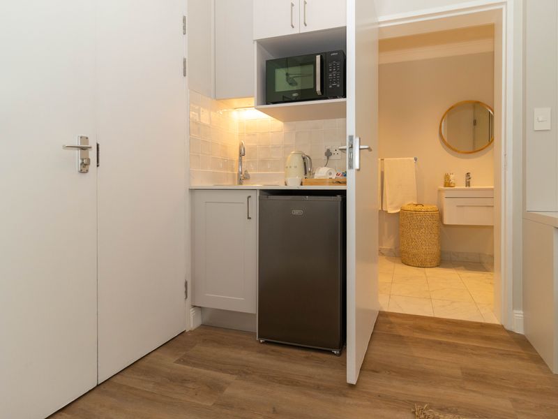 Compact kitchenette area featuring built-in cabinetry, under-counter sink, and integrated microwave, with direct access to an adjacent bathroom.
