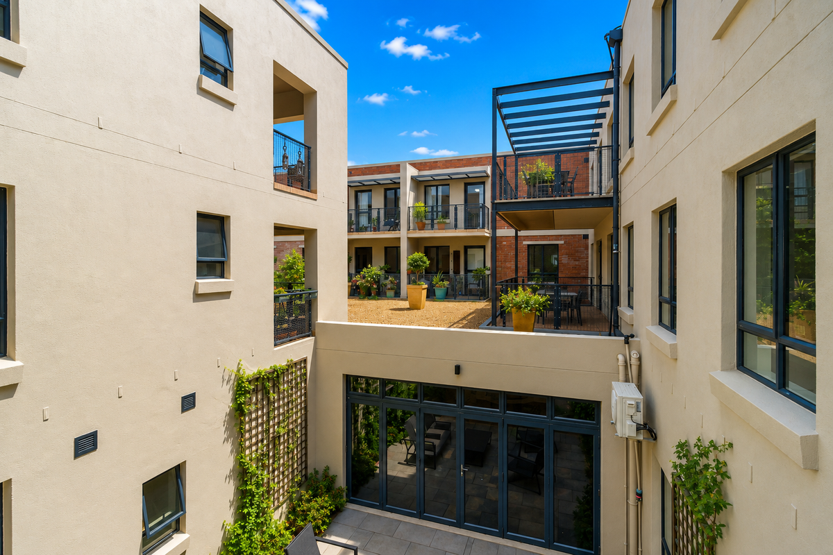 A view of the apartment complex courtyard featuring multi-level balconies, metal pergolas, paved patio areas, and modern bi-fold doors.