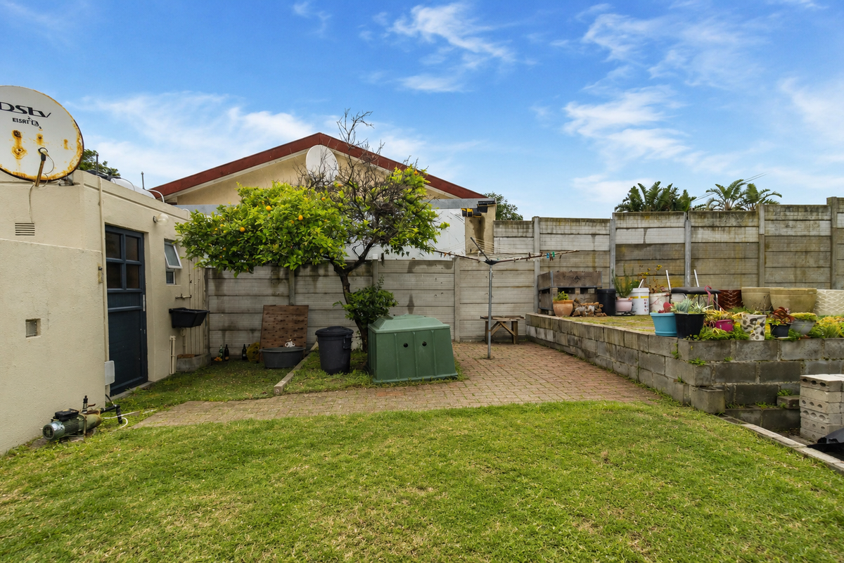 Rear garden area featuring a paved patio, lawn, and precast concrete boundary wall, providing a functional outdoor space with potential for landscaping improvements.