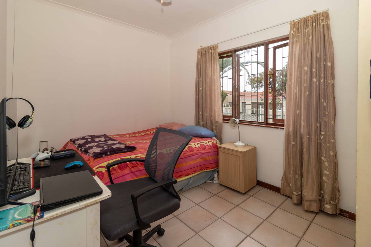 A functional bedroom featuring tiled flooring, a timber-framed window with security bars, and neutral wall finishes.