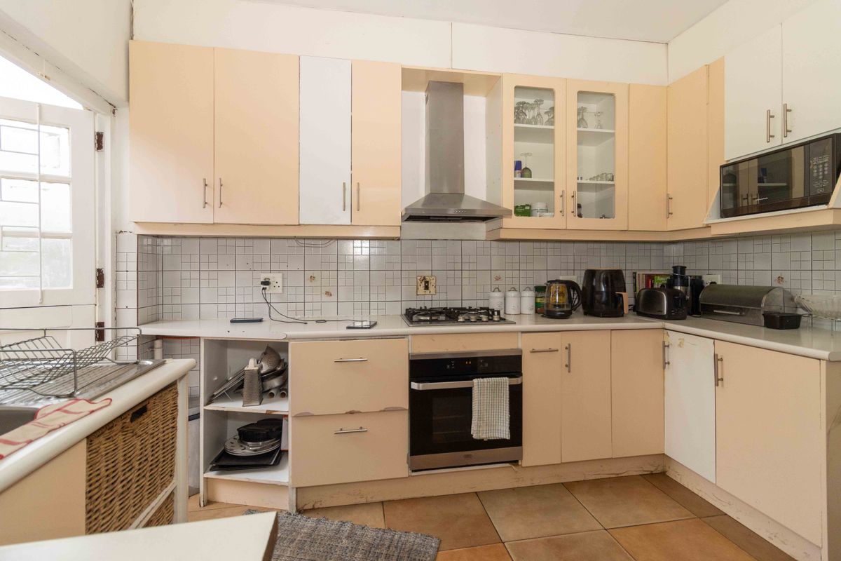A dated kitchen featuring built-in cabinetry, a gas hob, an integrated oven, and a stainless steel extractor fan, requiring cosmetic updates.