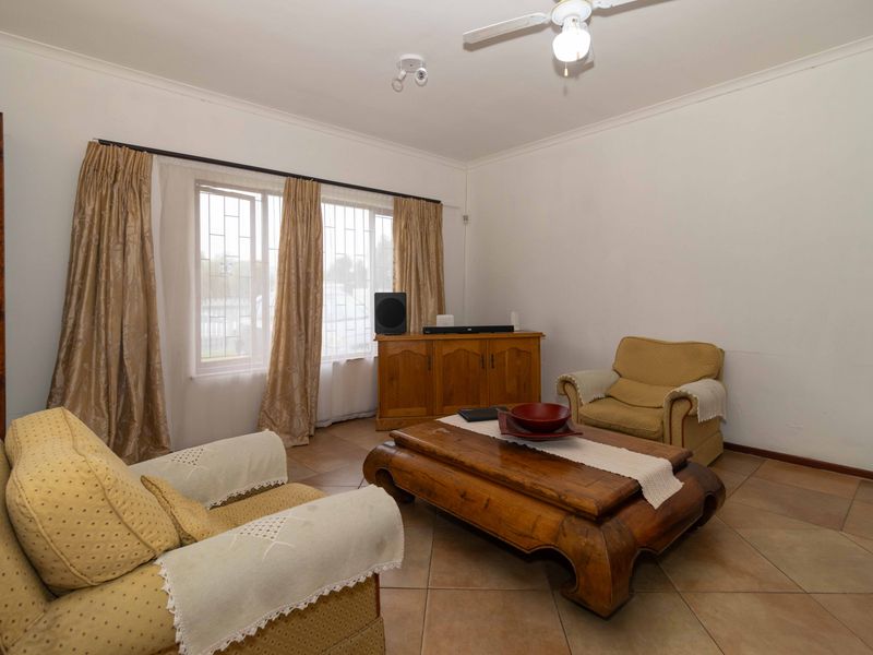 A comfortable living room featuring tiled flooring, a ceiling fan, and large windows fitted with security bars.