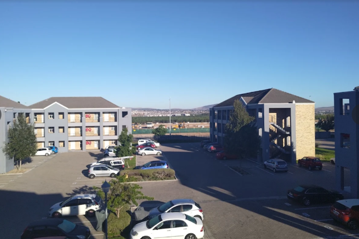 An elevated view of the apartment complex parking area, featuring paved surfaces, external staircases, and multi-story residential buildings.
