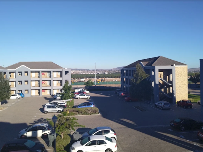 An elevated view of the apartment complex parking area, featuring paved surfaces, external staircases, and multi-story residential buildings.