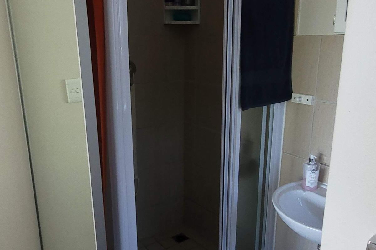 A functional bathroom featuring a shower enclosure with a built-in niche and a wall-mounted basin, finished with neutral floor and wall tiling.