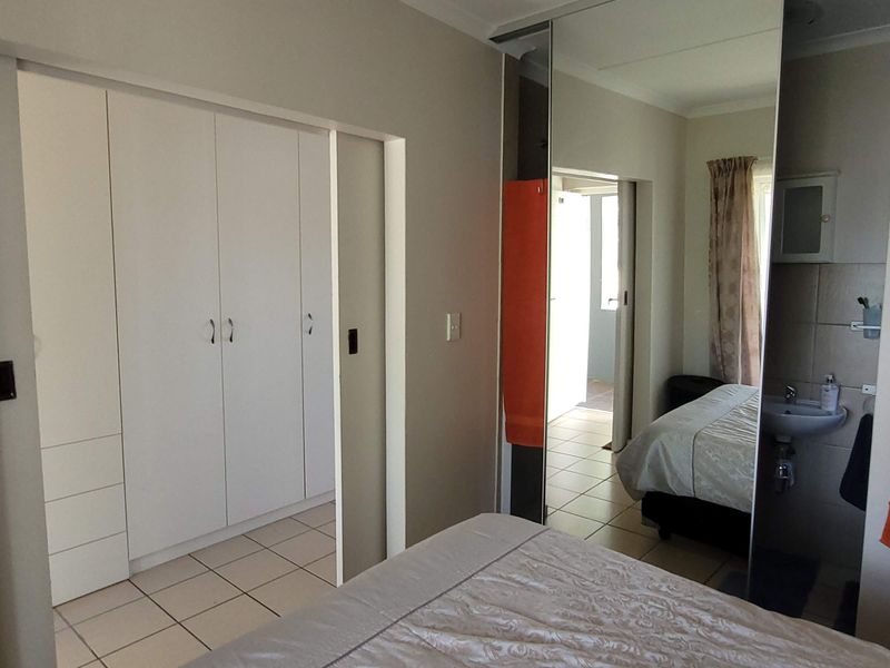 Bedroom featuring built-in cupboards with mirrored sliding doors, tiled flooring, and an integrated en-suite vanity basin area.