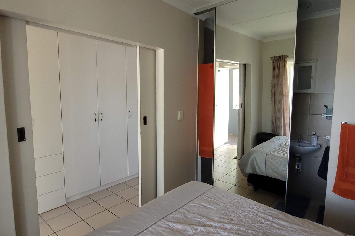 Bedroom featuring built-in cupboards with mirrored sliding doors, tiled flooring, and an integrated en-suite vanity basin area.
