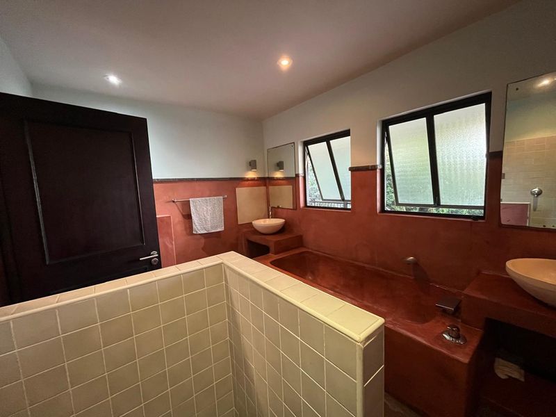 A bathroom featuring a built-in bathtub, dual vessel sinks, and a tiled partition wall with a distinct terracotta-colored finish.