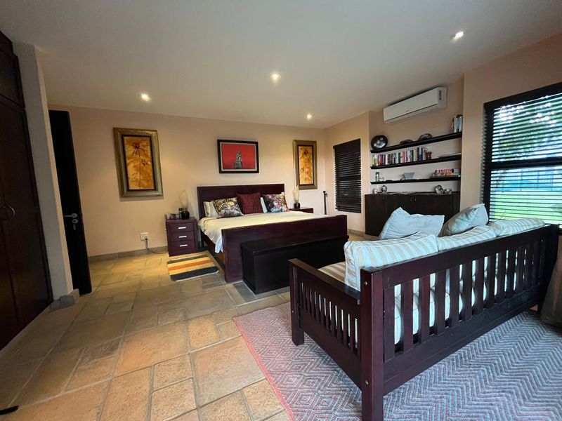 Spacious bedroom featuring stone tile flooring, built-in shelving, integrated cabinetry, and a wall-mounted split-system air conditioner.