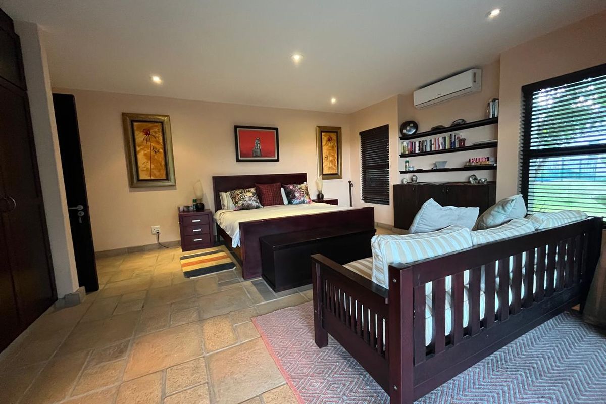 Spacious bedroom featuring stone tile flooring, built-in shelving, integrated cabinetry, and a wall-mounted split-system air conditioner.