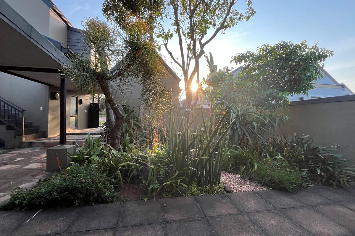 A private rear garden area featuring a paved patio, established landscaping, and a covered walkway leading to the main house structure.