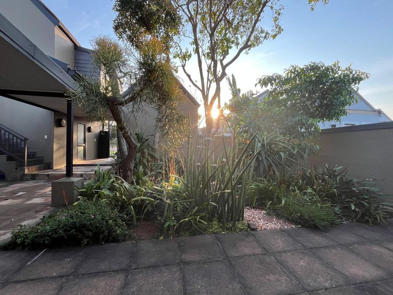 A private rear garden area featuring a paved patio, established landscaping, and a covered walkway leading to the main house structure.