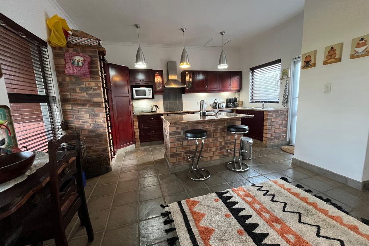 A rustic-style kitchen featuring brick cabinetry bases, stone countertops, a central island, and built-in appliances, finished with tiled flooring and pendant lighting.