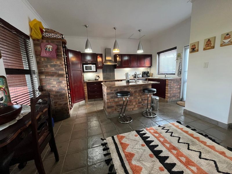 A rustic-style kitchen featuring brick cabinetry bases, stone countertops, a central island, and built-in appliances, finished with tiled flooring and pendant lighting.