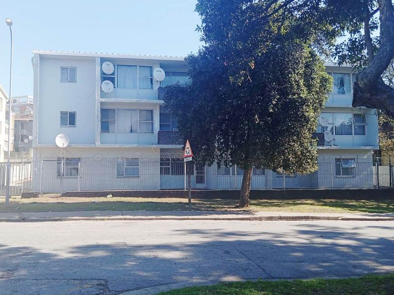 Front elevation of a multi-story apartment building featuring security fencing, razor wire, and multiple satellite dish installations.