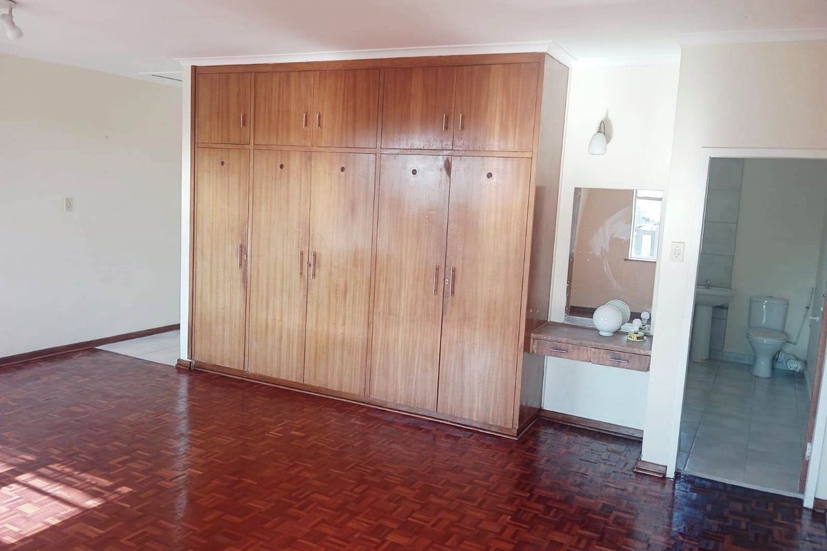 Spacious bedroom featuring classic parquet flooring, extensive built-in wooden cabinetry with an integrated vanity, and direct access to an en-suite bathroom.