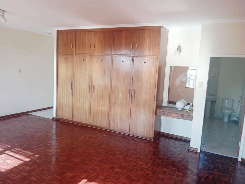 Spacious bedroom featuring classic parquet flooring, extensive built-in wooden cabinetry with an integrated vanity, and direct access to an en-suite bathroom.