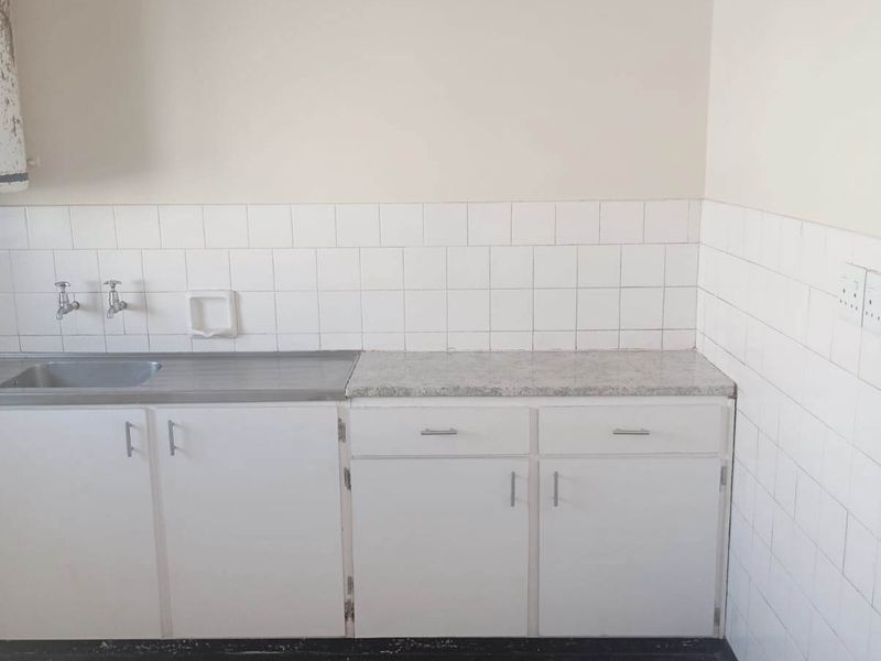 A compact, empty kitchen area featuring white cabinetry, a stainless steel sink, and tiled splashbacks, offering a blank canvas for potential renovation.