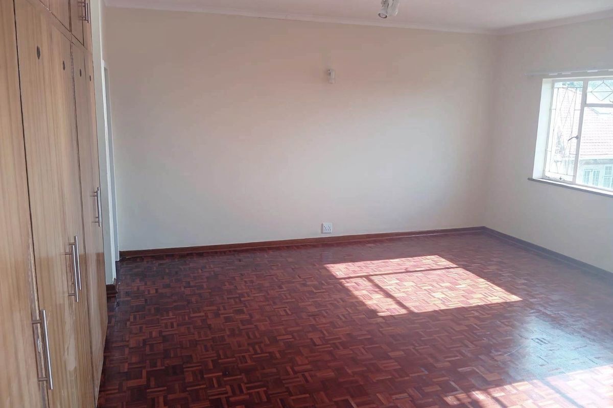 A spacious, empty bedroom featuring classic parquet flooring and extensive built-in wooden cupboards, offering a clean and neutral canvas for personalization.
