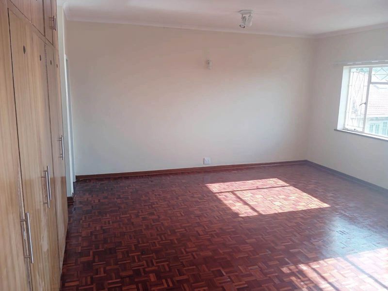 A spacious, empty bedroom featuring classic parquet flooring and extensive built-in wooden cupboards, offering a clean and neutral canvas for personalization.