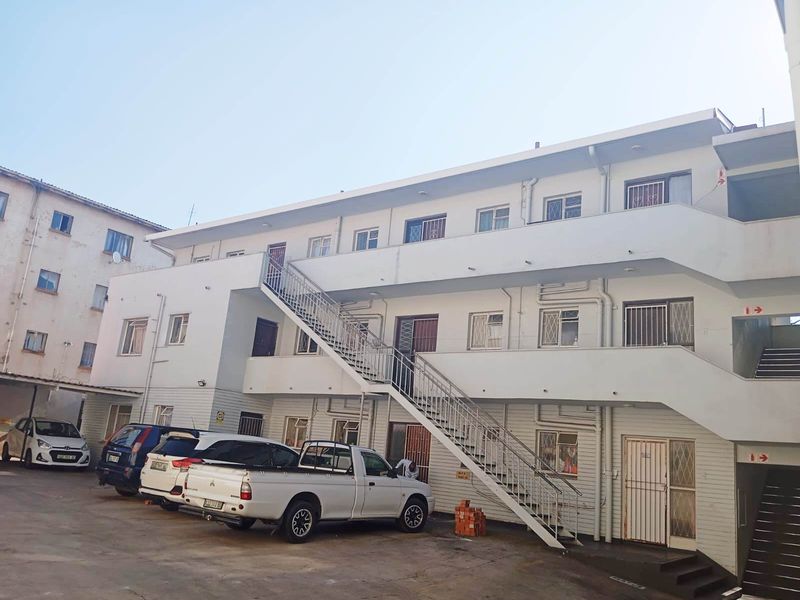 Exterior view of a multi-story apartment complex featuring an external staircase, security-fitted windows, and a paved parking area.