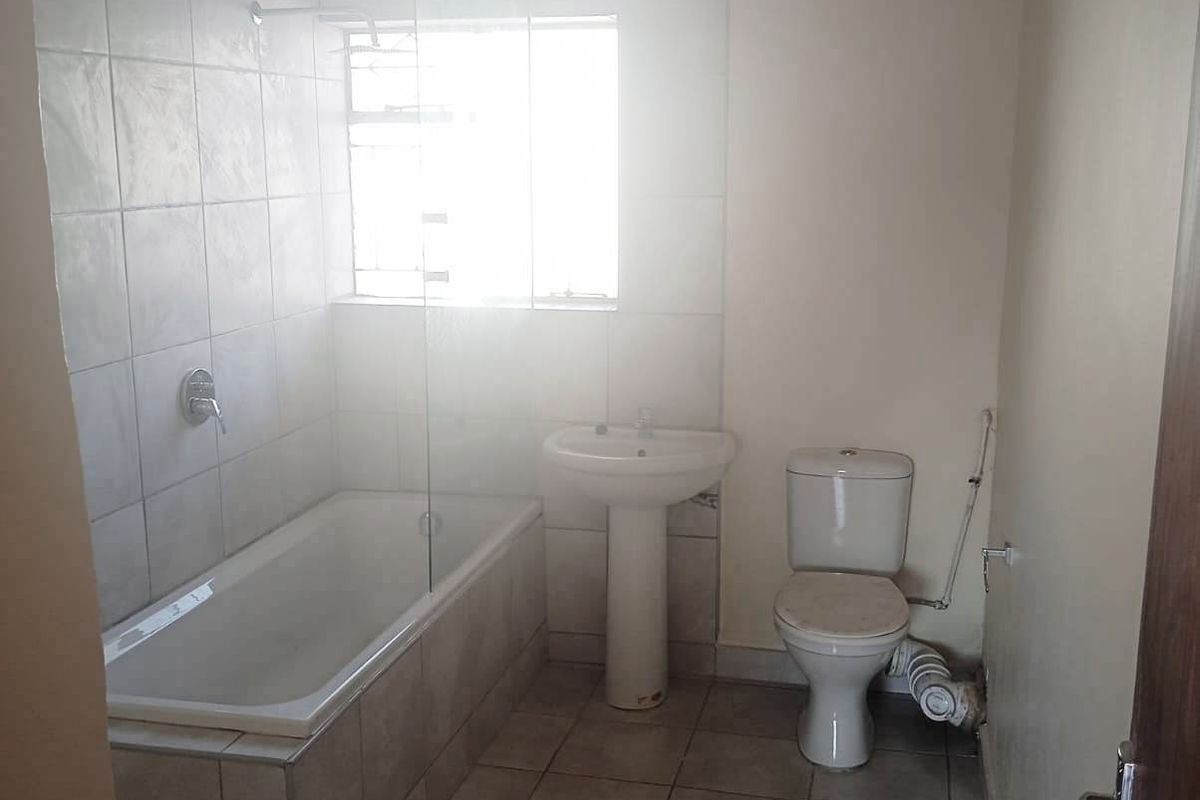 A functional bathroom featuring a pedestal basin, toilet, and a bathtub with a glass shower screen, finished with neutral wall and floor tiles.