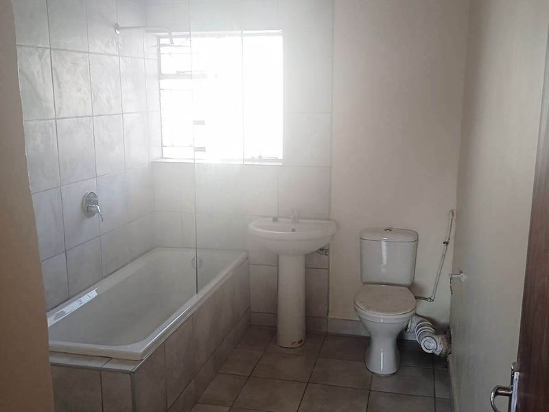 A functional bathroom featuring a pedestal basin, toilet, and a bathtub with a glass shower screen, finished with neutral wall and floor tiles.