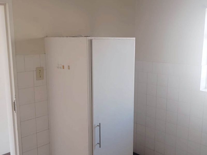 A small, functional kitchen area featuring tiled splashbacks, tiled flooring, and a single built-in cupboard unit.