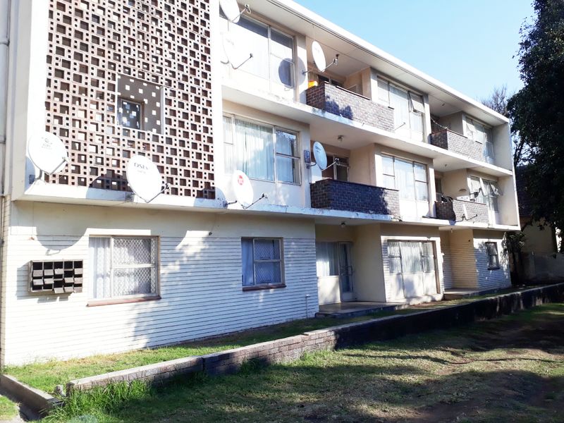 Exterior view of a multi-story apartment building featuring breeze block architectural details, private balconies, and a brick retaining wall along the front garden area.